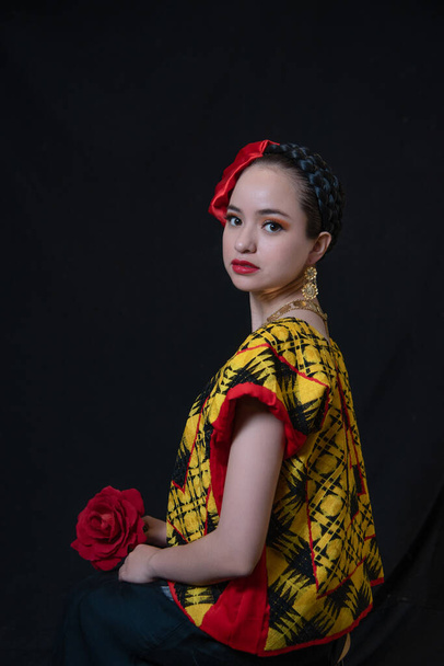 Tehuana gibi giyinmiş, Meksika Oaxaca 'dan kesilmiş, kırmızı çiçekli, altın kolyeli, küpeli, siyah arka planlı, gülümseyen ve düşünceli bir Latin kadın. - Fotoğraf, Görsel