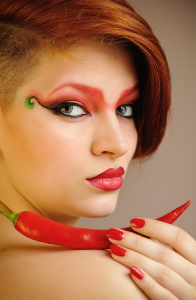 Porträt einer schönen Frau mit kreativem roten Make-up hält Chilischoten - Foto, Bild