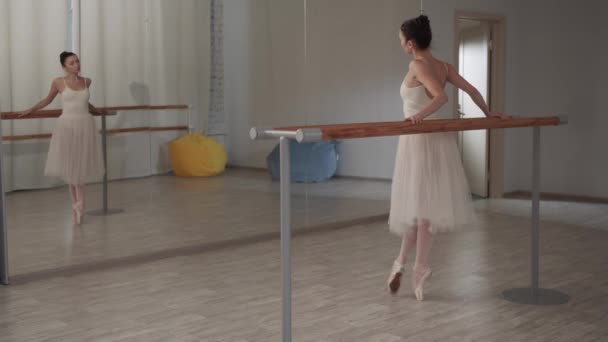 Очаровательная балерина перед зеркалом на репетиции тянет ногу высоко, помогает рукой - Кадры, видео