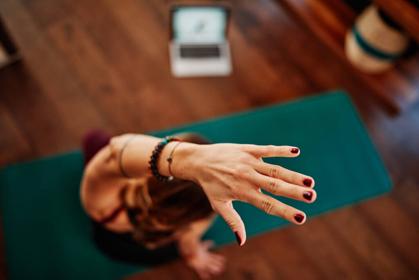 Een vrouw van middelbare leeftijd doet yoga, na een online tutorial op laptop tijdens corona virus pandemie. - Foto, afbeelding