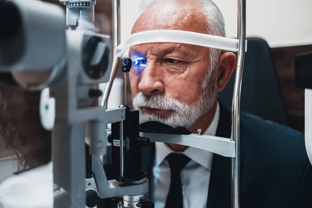 Elegant senior bearded man receiving ophthalmology treatment. Doctor ophthalmologist checking his eyesight with modern equipment. - Foto, Bild