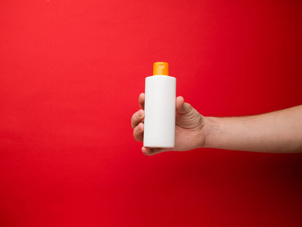 Mão segurando frasco de xampu isolado no fundo vermelho. - Foto, Imagem
