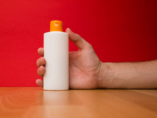 Рука тримає пляшку шампуню ізольовано на червоному тлі
. - Фото, зображення