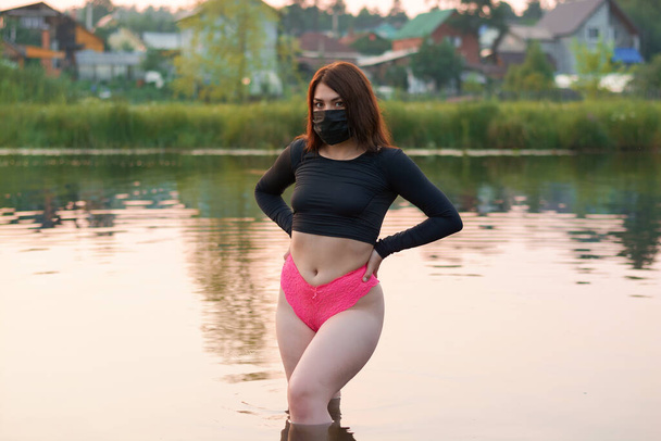 een mooie vrouw met een zwart medisch masker staat in de rivier.rest in de pandemie. - Foto, afbeelding