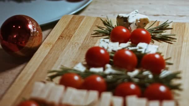 Plat leggen van kaas en tomaten. Stukjes kaas, tomaten en rozmarin in de vorm van een kerstboom. Eten voor kerstvakantie. Rotatie. Langzame beweging - Video