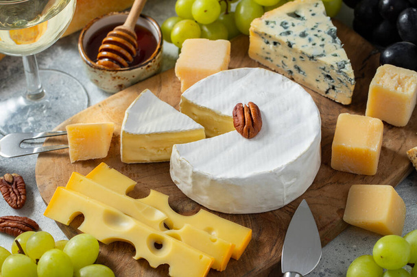 Tasting cheese dish on a wooden plate. Food for wine and romantic date, cheese delicatessen on a light concrete background - Photo, Image