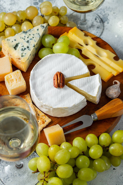 Tasting cheese dish on a wooden plate. Food for wine and romantic date, cheese delicatessen on a light concrete background - Foto, imagen