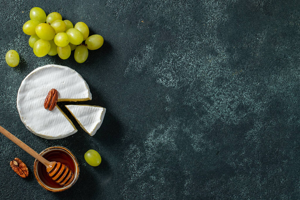 Tasting cheese dish on a wooden plate. Food for wine and romantic date, cheese delicatessen on a black concrete background. Top view with copy space. - Foto, Imagen