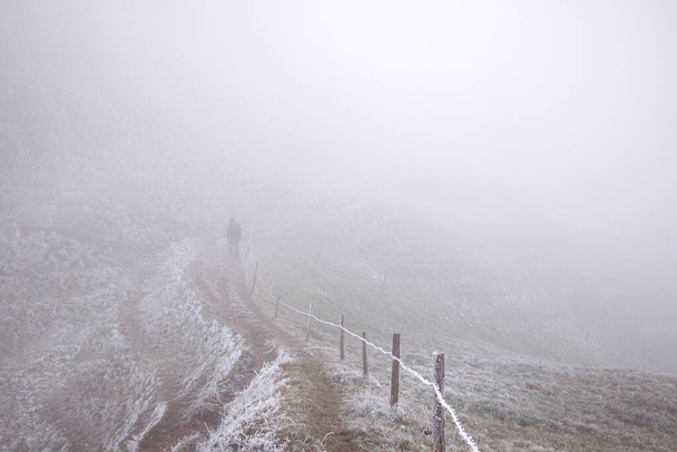 Muž kráčející v mlze. Zimní krajina s figurkou na stezce pěší turistika na horské stezce při nízké teplotě. Wanderer koncept. - Fotografie, Obrázek
