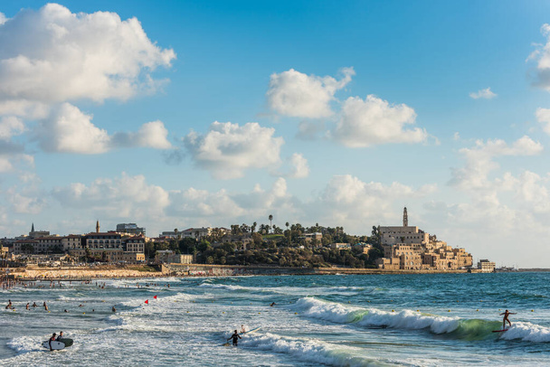 Old Jaffa city, old port and coastal line of Tel Aviv under sunset and lots of tourists are swimming and surfing at the Mediterranean sea. - Foto, imagen