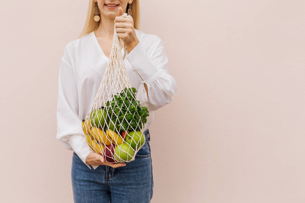 Reusable eco bag for shopping. String shopping bag with fruits in the hands of a young woman. Zero waste, plastic free concept. Eco lifestyle. Eco shopping. Conscious consumption. Eco trend.Copy space - Valokuva, kuva