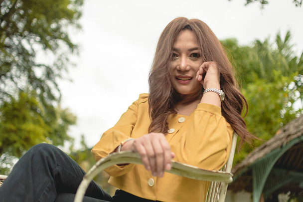 Eine erfolgreiche Südostasiatin lümmelt auf einem Stuhl vor ihrer Villa und blickt in die Kamera. Erfolgreich, etabliert und reich. - Foto, Bild