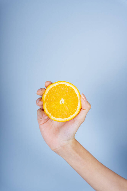Main de femme tenant une tranche d'orange sur fond bleu. - Photo, image