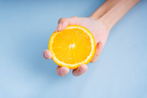 青の背景にオレンジのスライスを保持する女性の手. - 写真・画像