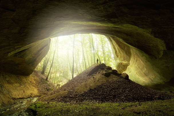 Cave entrance with man standing in front and sun shining - Photo, Image