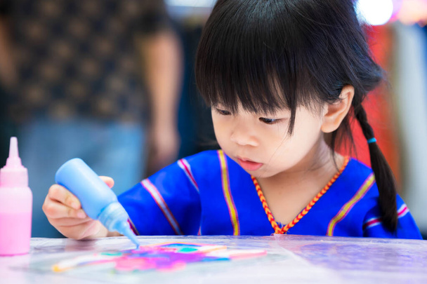 Menina asiática bonito está trabalhando na arte na forma de cair aquarelas de uma garrafa em uma peça de trabalho. Menina feliz vestindo uma camisa azul tem 3-4 anos. - Foto, Imagem