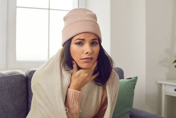 Ongelukkig zieke jonge vrouw in warme kleren die lijden aan griep en klagen over keelpijn - Foto, afbeelding