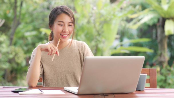 Freelance Aziatische vrouw die thuis werkt, zakenvrouw die 's morgens op een laptop in de tuin zit. Lifestyle vrouwen werken thuis concept. - Foto, afbeelding