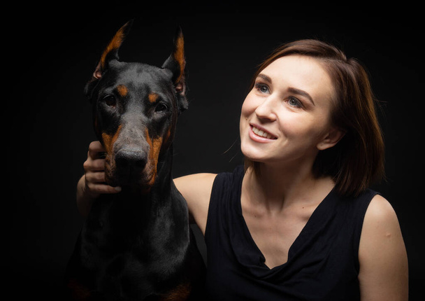 Portrait of a Doberman dog with a girl owner. Isolated Studio photo on a black background. - Photo, Image