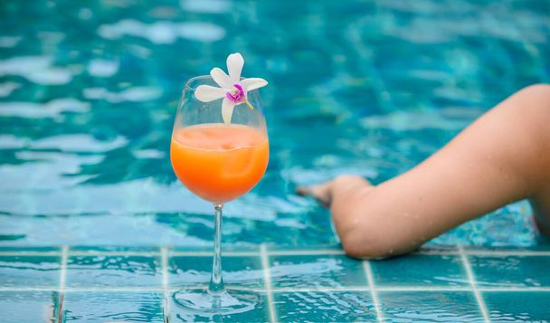 Frau trinkt ein Cocktailglas Orangensaft im Schwimmbad. Sommerurlaub und allein zu Hause entspannen. - Foto, Bild