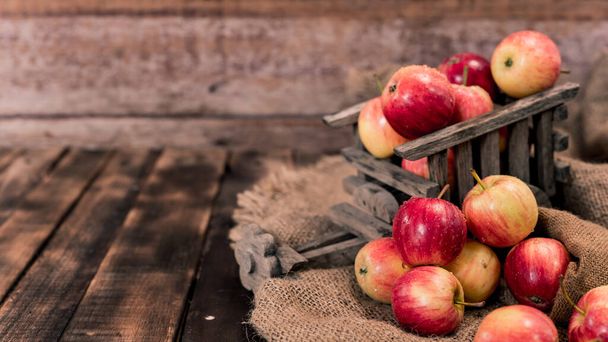 木製の箱に有機熟した赤いリンゴ。秋にはトウモロコシの収穫があります。木のテーブルの背景を持つ新鮮な果物. - 写真・画像