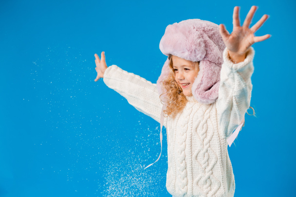 carino bambina in rosa peloso cappello giocare con finta neve su sfondo blu in studio - Foto, immagini