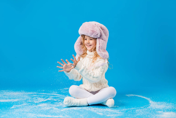 felice bambina in abiti invernali con neve finta sul backgorund blu - Foto, immagini