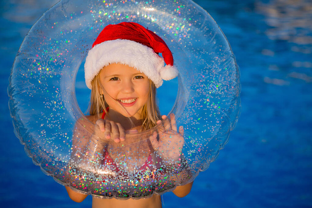 smiling little girl in christmas hat holding swimming circle by pool - Photo, Image