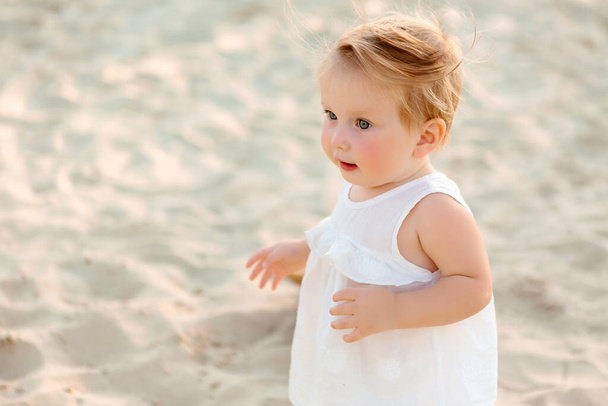 cute toddler girl in white dress with sand on background - Foto, Imagem