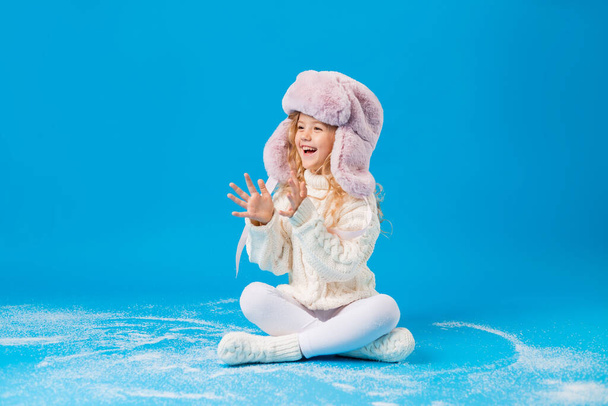 happy little girl in winter clothes with fake snow on blue backgorund - Foto, Imagem