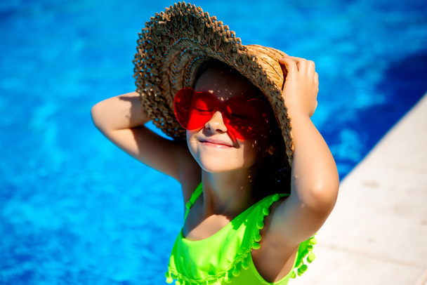 menina bonito em chapéu de palha e óculos em forma de coração posando por piscina - Foto, Imagem