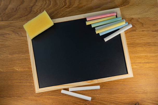 Crayons lie on a black chalkboard on the surface of an oak table. Creative concept. - Fotoğraf, Görsel