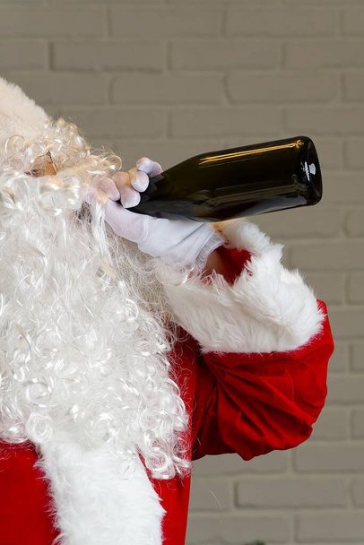 Le Père Noël boit du vin mousseux dans une bouteille. ivre santa claus concept - Photo, image