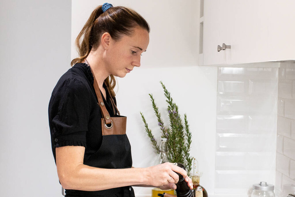 Młoda piękna kobieta stoi przy piecu i tarcie sera dla zdrowego przepisu żywności. Urocza Norweżka pracująca jako bloger kulinarny i trener stylu życia przygotowująca jedzenie w kuchni. - Zdjęcie, obraz