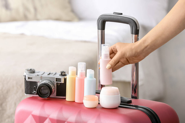 Female hand, set of travel bottles with body care cosmetics and photo camera on packed suitcase - Foto, afbeelding