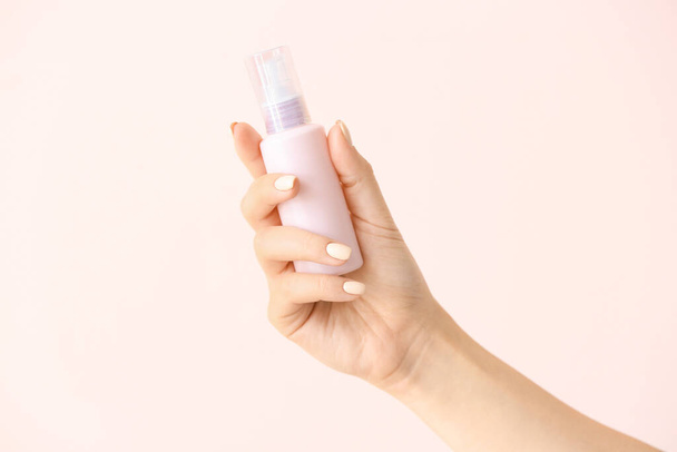 Female hand and travel bottle with body care cosmetics on light background - Foto, Imagen