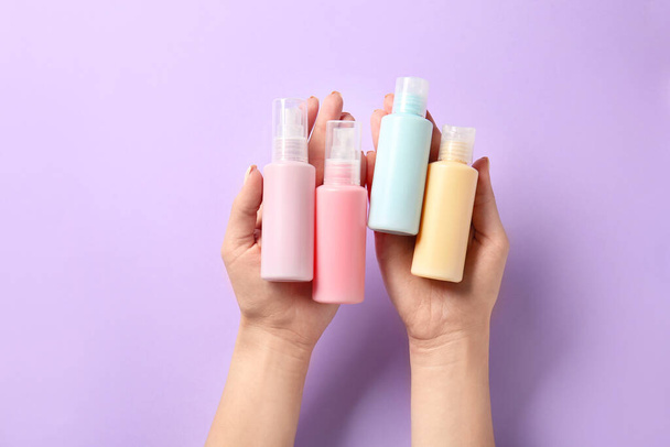 Female hands and travel bottles with body care cosmetics on color background - Photo, Image