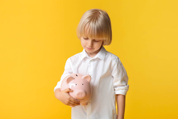 Netter kleiner Junge mit Sparschwein auf farbigem Hintergrund - Foto, Bild