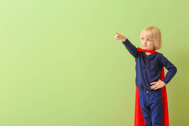 Little boy dressed as superhero showing at something on color background - Foto, Bild