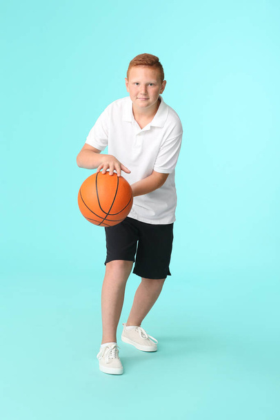 Sporty teenage boy playing basketball on color background - Foto, Bild