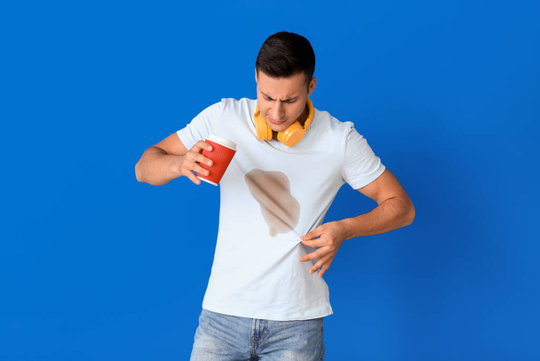 Stres mladý muž s kávovými skvrnami na jeho t-shirt na barevném pozadí - Fotografie, Obrázek