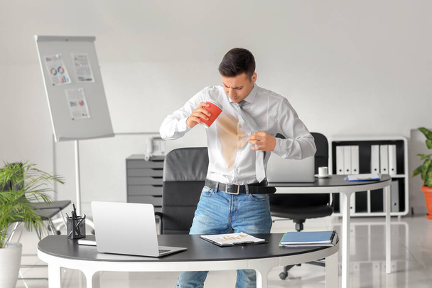 Napjatý mladý podnikatel s skvrnami od kávy na košili a psacím stole v kanceláři - Fotografie, Obrázek