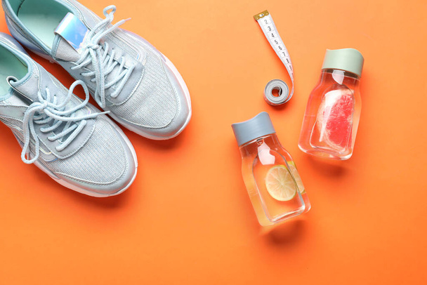 Flessen van geïnfundeerd water, sportschoenen en meetlint op kleur achtergrond - Foto, afbeelding