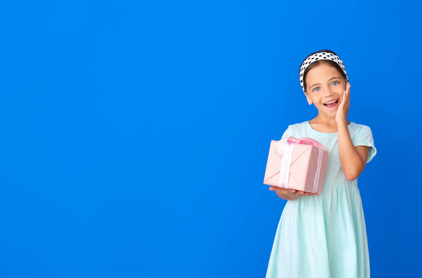 Happy little girl with gift on color background - Photo, Image