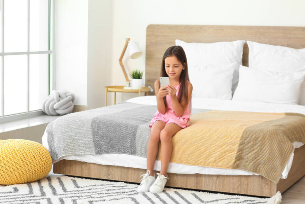 Roztomilá holčička s mobilním telefonem v ložnici - Fotografie, Obrázek