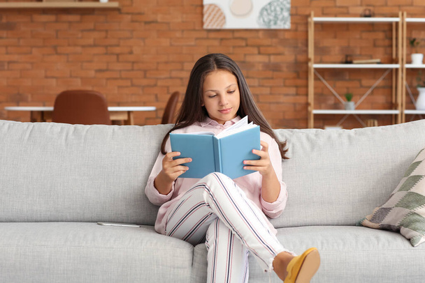 Cute teenage girl reading on sofa at home - 写真・画像