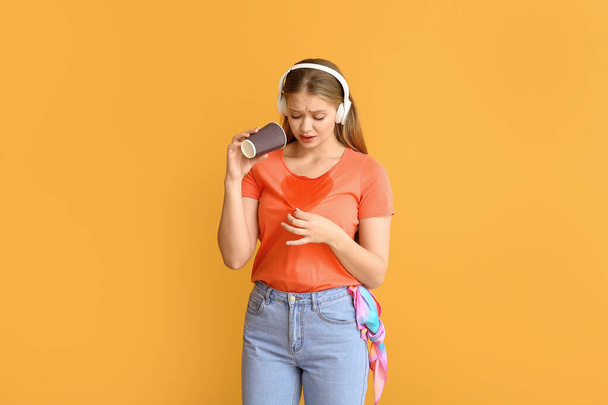 Young woman with coffee stains on her t-shirt and headphones on color background - Foto, immagini
