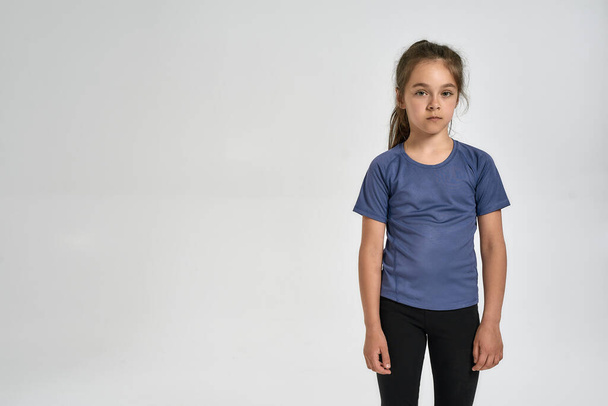 Little sportive girl child in sportswear looking at camera, while standing isolated over white background - Foto, immagini