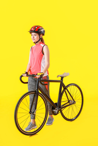 Female cyclist with bicycle on color background - Photo, Image