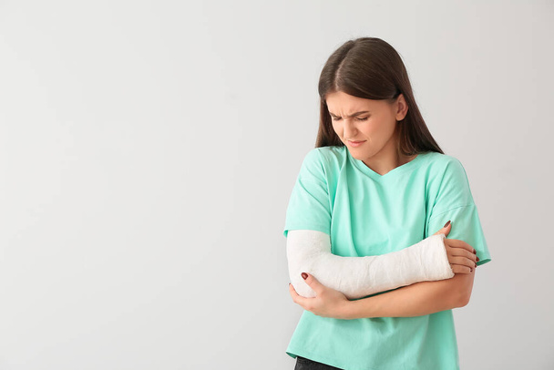 Young woman with broken arm on light background - Φωτογραφία, εικόνα